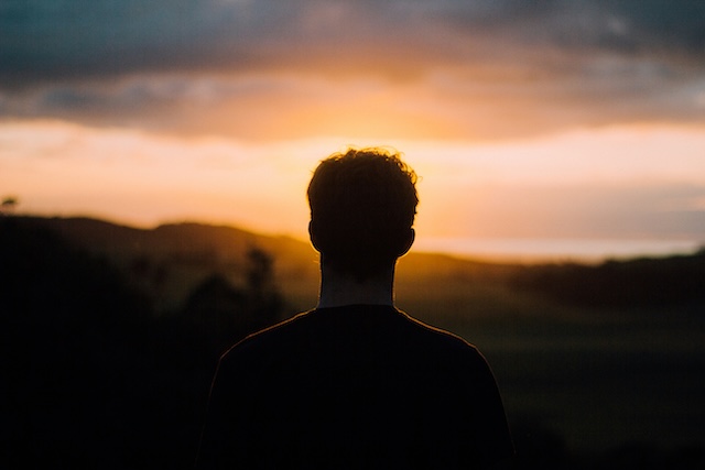 The silhouette of a man's head and shoulders standing towards the sunset